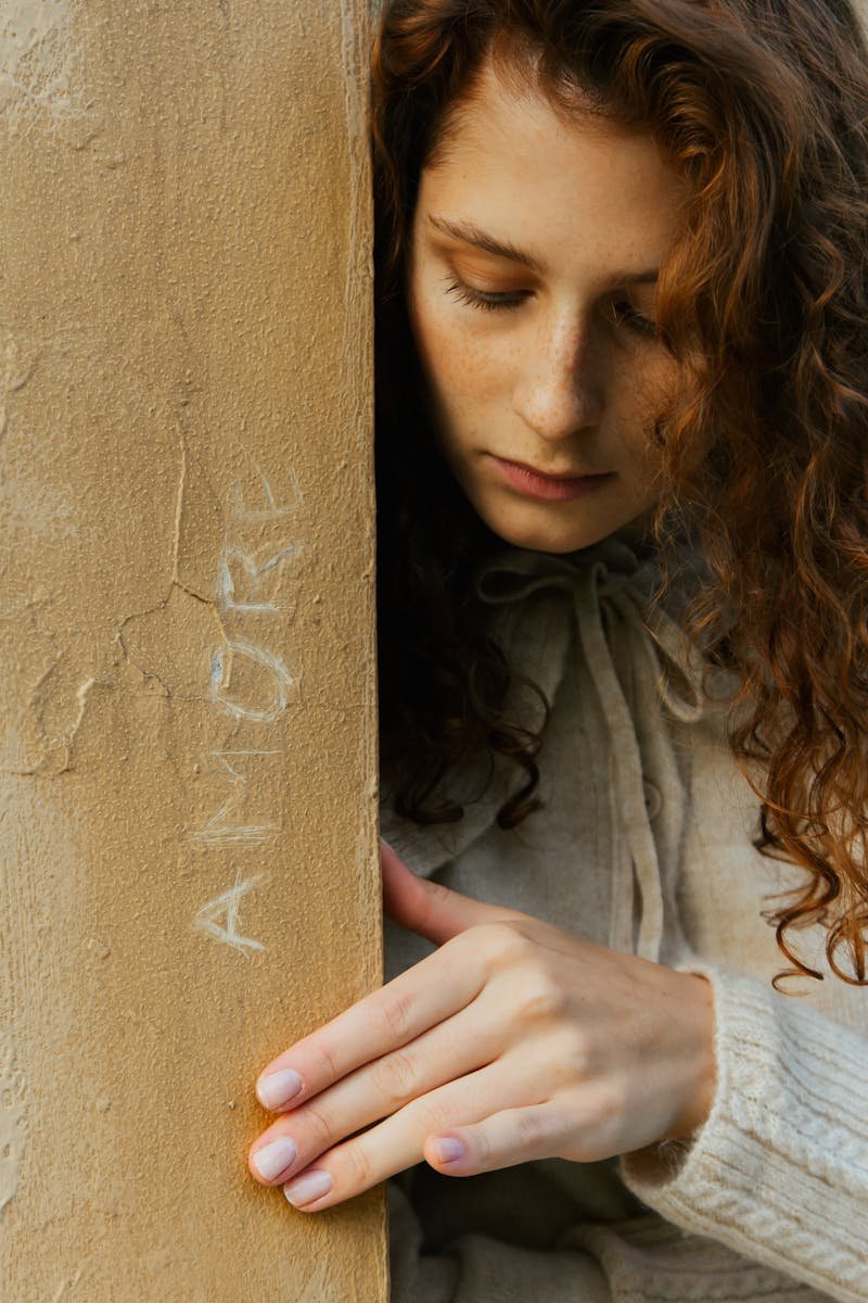 A young woman with curly hair in contemplation beside a column inscribed with 'amore'.