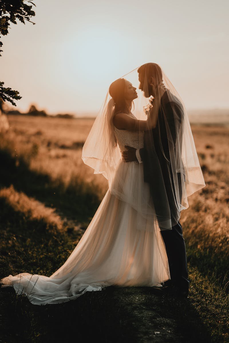 Bride and groom share a romantic moment at sunset in a scenic field.