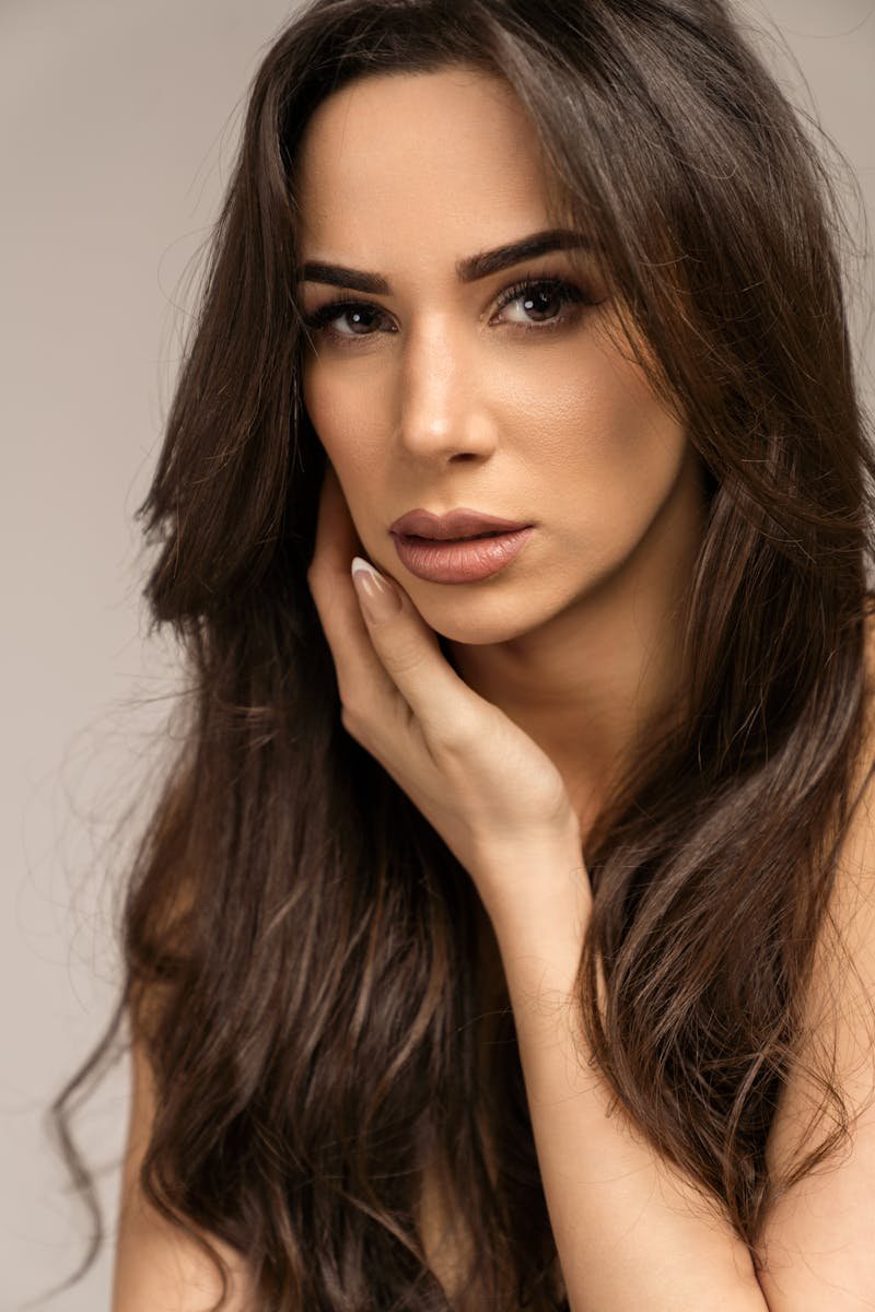 Photo by Lazarus Ziridis Close-up portrait of a woman with long brunette hair and soft makeup, looking at the camera.