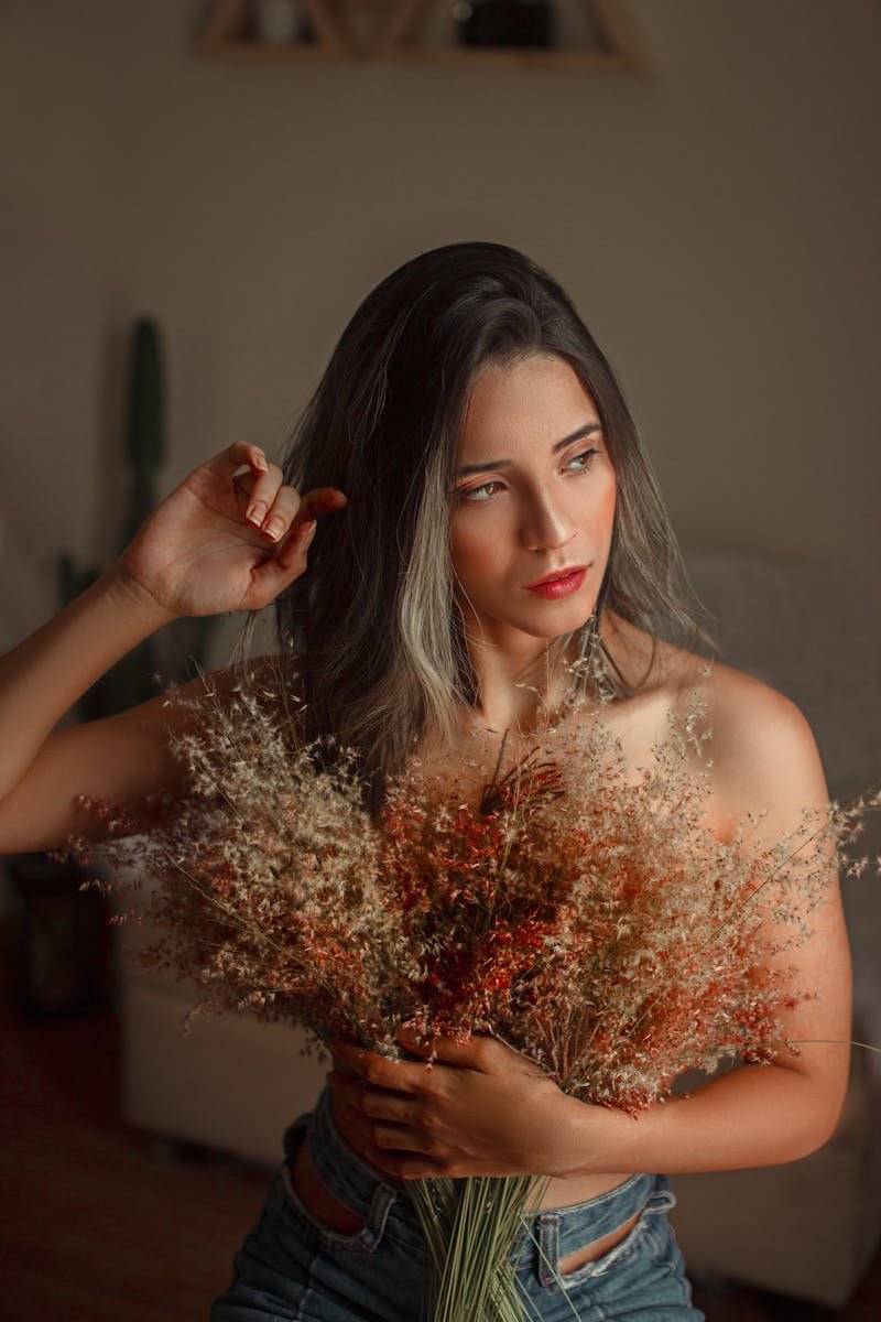 Woman poses indoors holding a bouquet of dried flowers, capturing a warm and intimate mood.