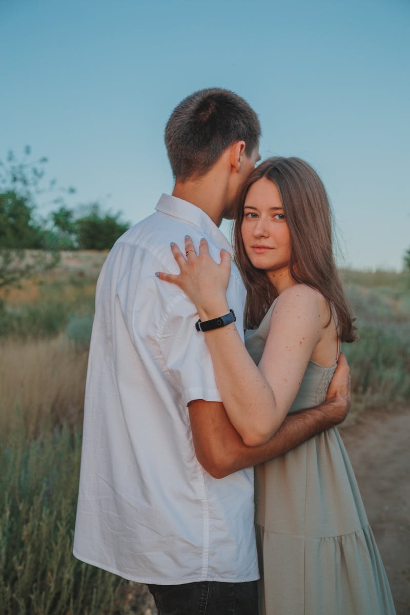 Content woman embracing anonymous man while standing on sandy road in countryside against blue sky in summer day in nature