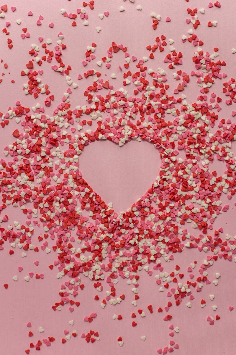 Heart-shaped confetti arrangement on a pink background, ideal for romantic and festive occasions.