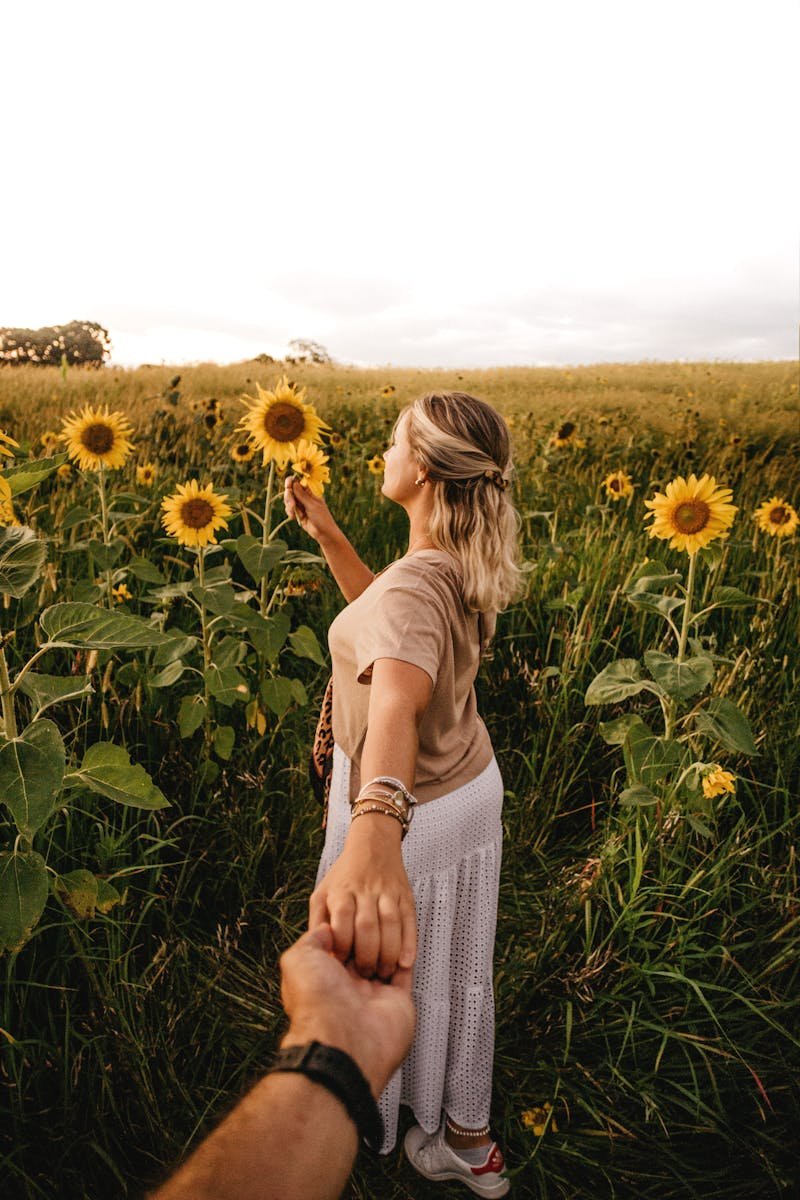 Photo by Jonathan Borba A couple holding hands in a blooming sunflower field during a serene summer sunset.