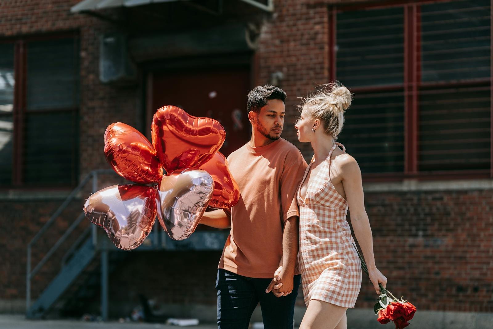 Young couple walks hand in hand outdoors with heart-shaped balloons.