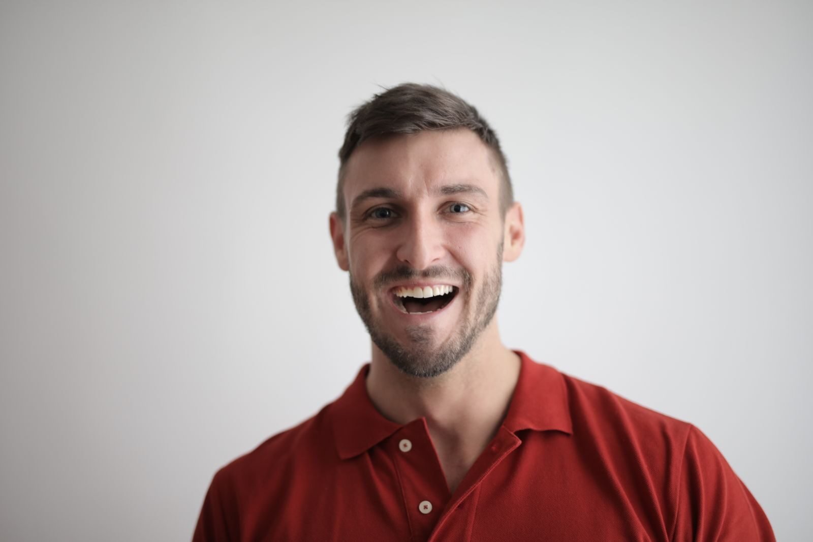 Photo by Andrea Piacquadio A cheerful man smiling broadly in a red polo shirt against a white background.